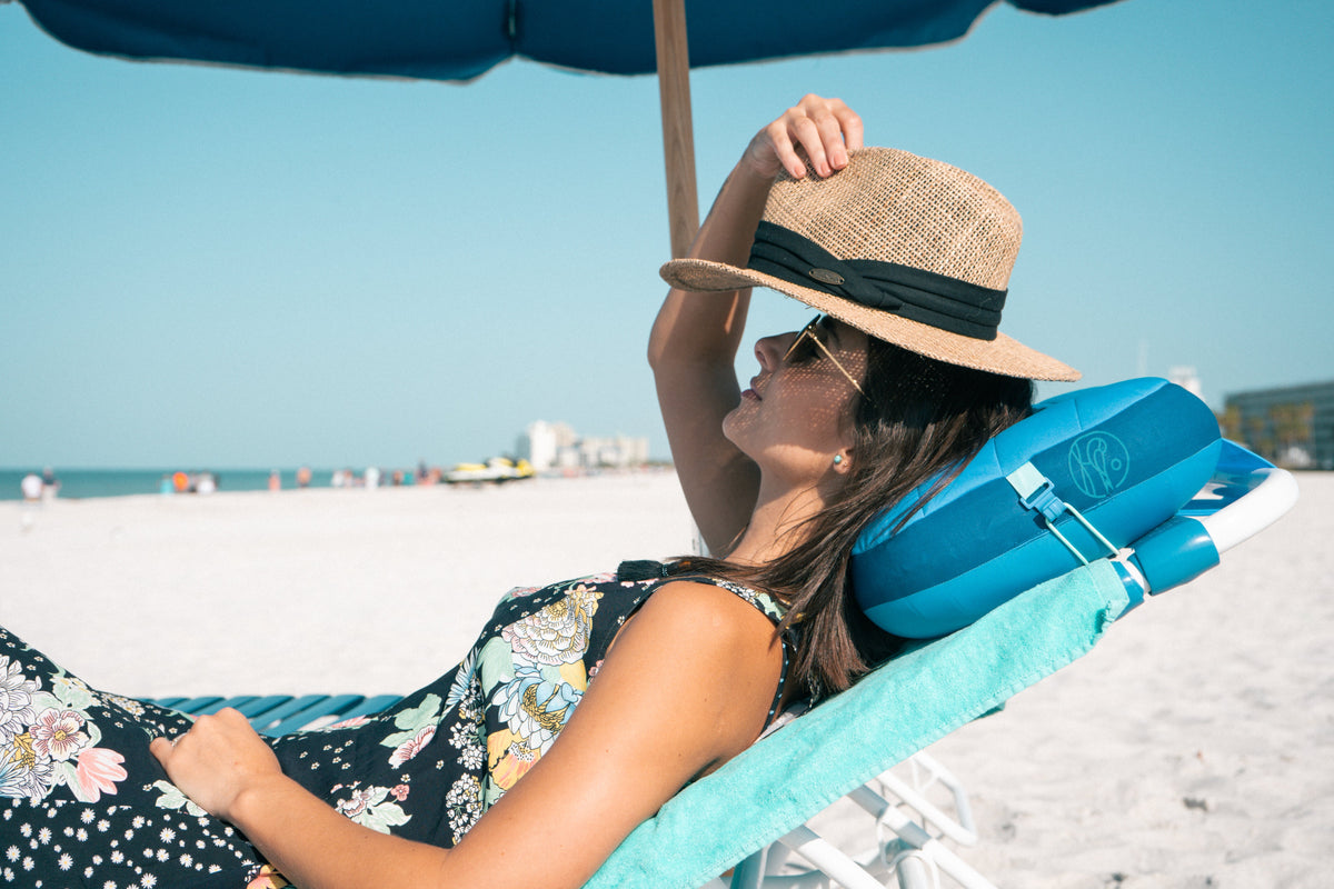 woman sitting at the beach on a chair with a blue beach pillow under her head